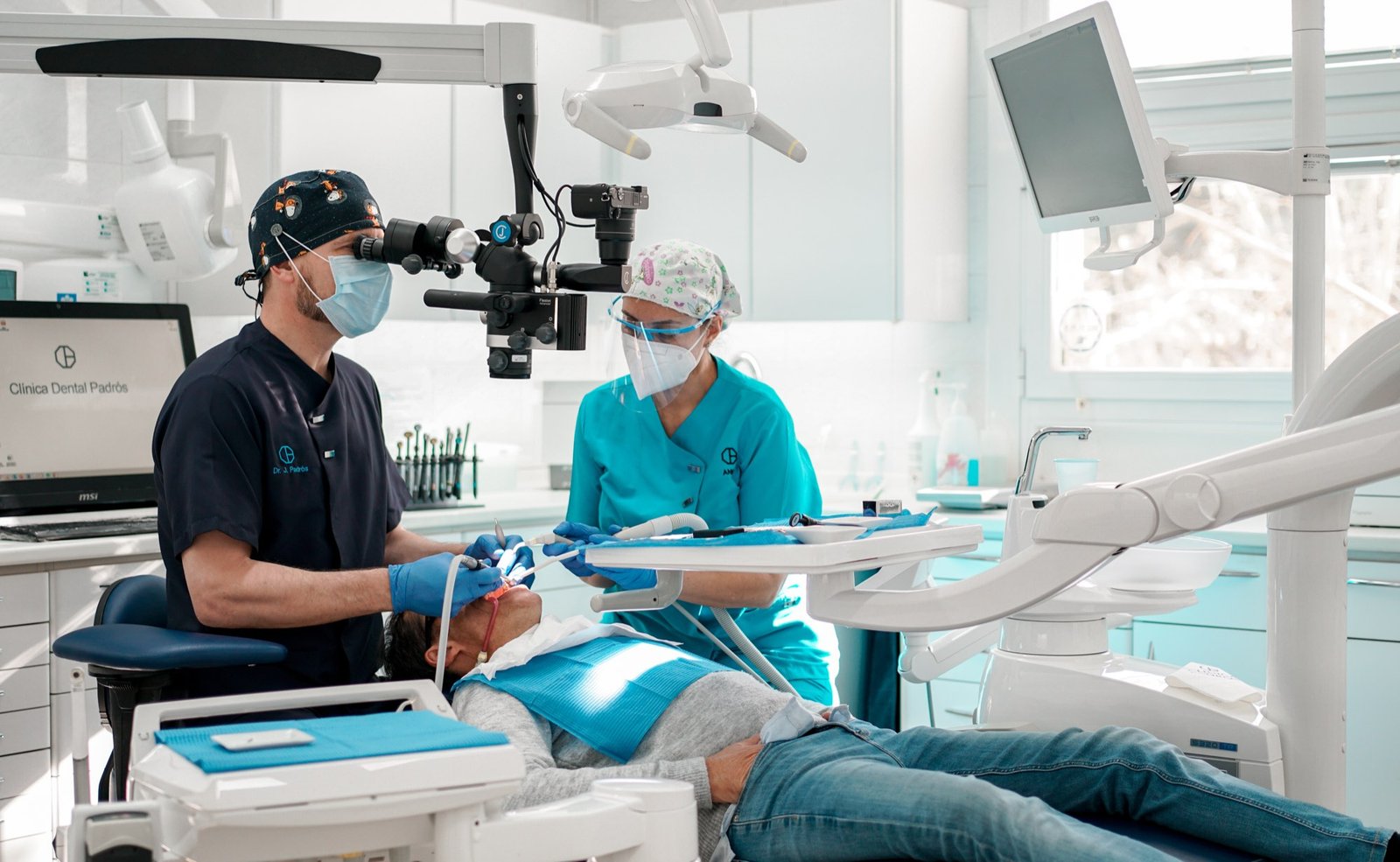 Dos profesionales de Clínica Dental Padrós Paralelo tratando a un paciente en consulta, con el logotipo de la clínica visible en pantalla